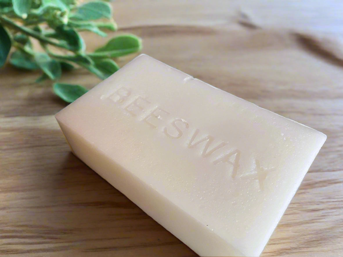 A jar of wax melts labeled 'Soli Deo Gloria' with a heart design, alongside a black lid, a piece of ice with a wax melt on it, and scattered coffee beans on a wooden surface, all indicating a vanilla scent.