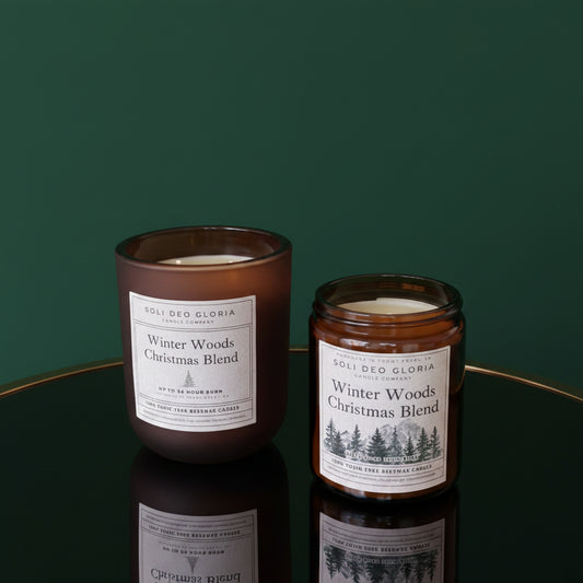 Two candles labeled 'Winter Woods Christmas Blend' on a wooden surface with a snowy window background.