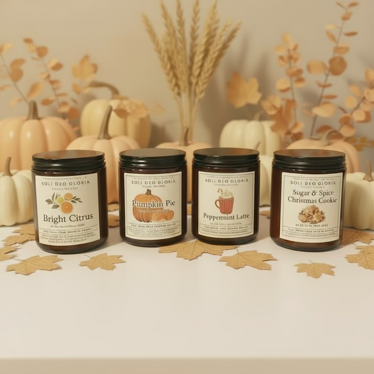 Four candles with labels on a wooden surface in front of a decorated Christmas wreath.