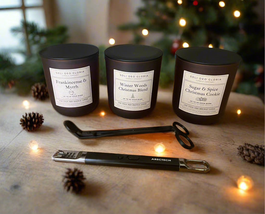 Three candles with labels on a wooden surface with Christmas decorations in the background