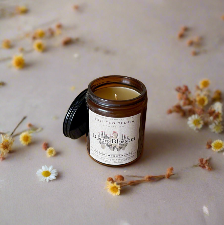 Beeswax candle in an amber jar with a label with Desert Blossom on the outside and flowers sprinkled around.