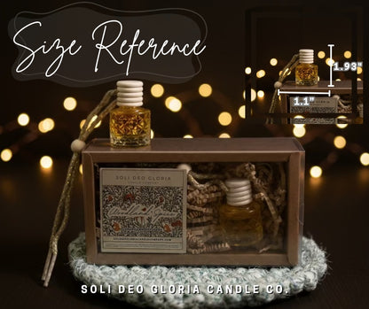 A product presentation for a SOLI DEO GLORIA candle, showing a brown wooden display box with a clear window, a small glass bottle with a white wick, and decorative rope. An inset diagram in the top right shows the bottle dimensions (1.