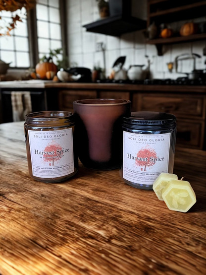 Two candles labeled 'Harvest Spice' on a wooden surface with a kitchen background.