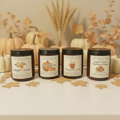 Four candles with labels on a wooden surface in front of a decorated Christmas wreath.