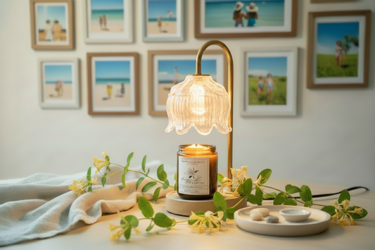 Candle with decorative lamp and greenery on a table against a wall with framed pictures.