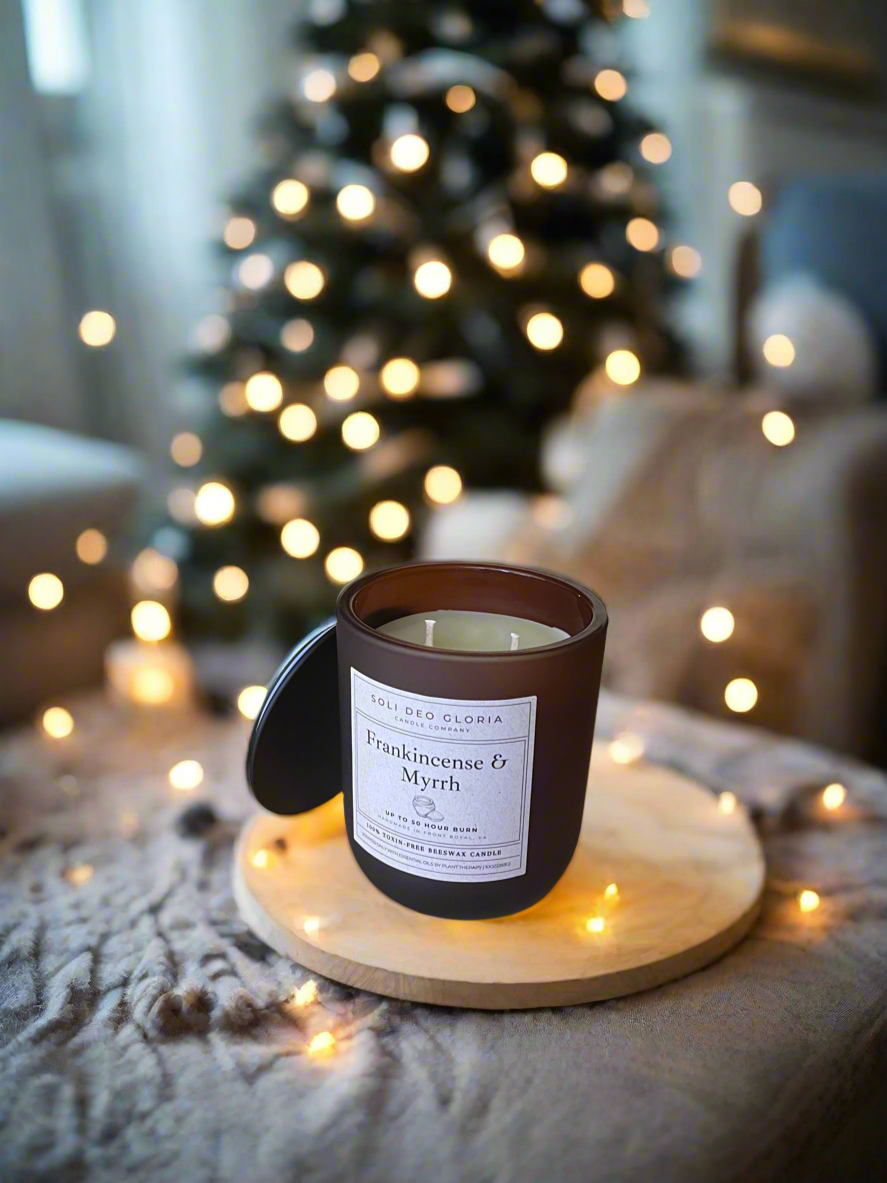 Candle with a label on a wooden coaster in front of a decorated Christmas tree.