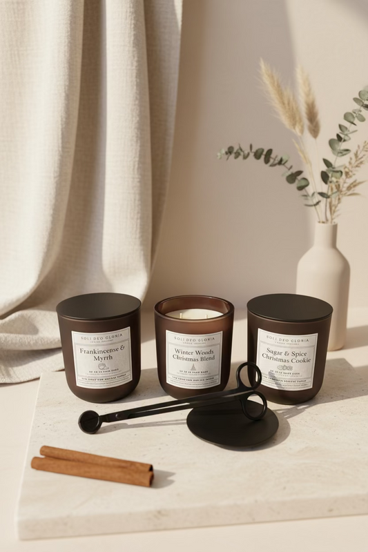 Three candles with labels on a surface with a vase and cinnamon sticks in the background.